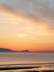 Fototapeta premium Sunset over the Firth of Clyde taken from Prestwick beach, with north end of Arran silhouetted against the sunset sky and figures at the water's edge