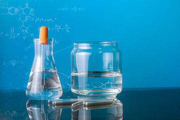Group of laboratory flasks empty or filled with a clear liquid on blue tint scientific graphics background and their reflection on a table
