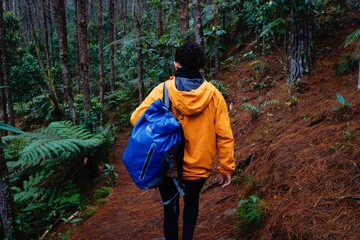 Young woman in yellow jacket and blue backpack walking through the forest