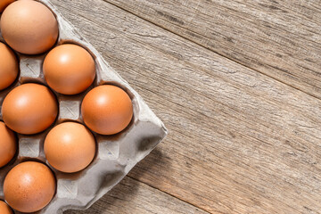 Chicken eggs in a cartoon with a copy space on wooden board background. Flat lay.