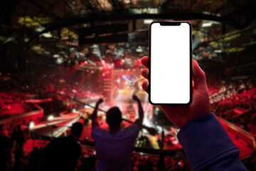 Gamer using smartphone during big esports gaming event sitting on the tribunes inside the arena. Blank screen with copy space mockup - 410670964