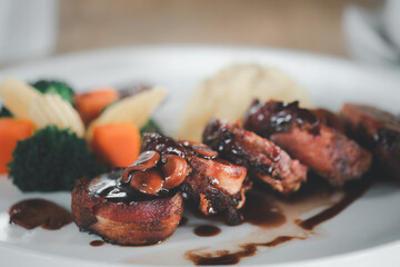 Bacon-wrapped pork fillet on white dish served on cooked vegetable