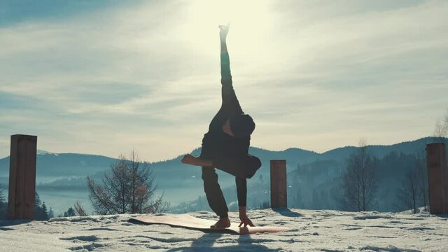 Caucasian senior man doing yoga exercises in front of amazing sunset on the winter mountains