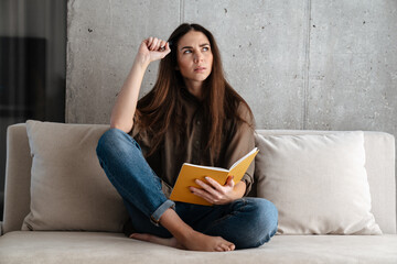 Brooding brunette nice girl writing down notes while sitting on sofa