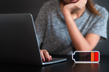 Young tired woman working on laptop at home . low battery signal . 