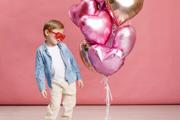 Boy dancing, smiling and having fun near  big branch of pink heart-shaped ballons. Isolated on pink...