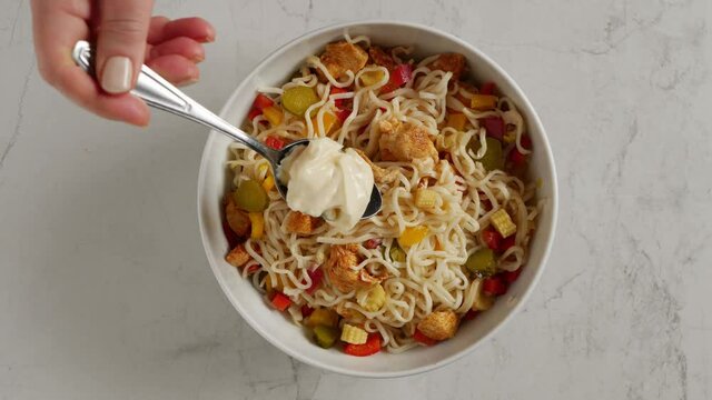 Chinese noodle salad. The cook puts a tablespoon of mayonnaise on the salad. Slow motion. View from above.