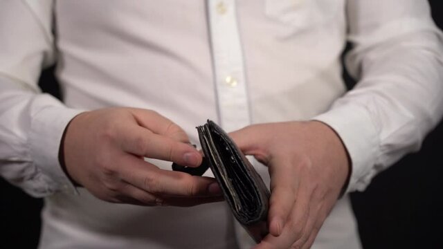 A man in a white shirt on a black background shows an empty, leaky old wallet. Financial Problems Concept