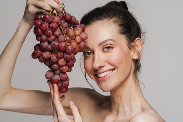 Smiling half-naked woman posing with bunch of grapes