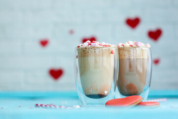 Two glasses of hot coffee or cappuccino with marshmallows and heart-shaped cookies on a blue background.