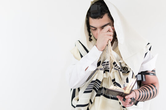 Young Orthodox Jewish man in shawl (tallit) and phylacteries (tefilin), praying with a prayer book (sidur).