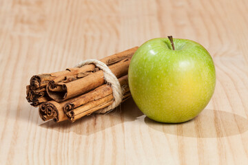 Green apple with a cinnamon stick; photo on wooden background.