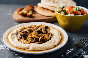 Hummus with fried mushrooms, cucumber and tomato salad, falafel and pita. Dark background. Middle Eastern dish