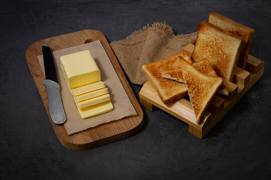 A piece of butter, sliced, on a cutting board, with toast bread, on a black background, no people, horizontal,top view,
