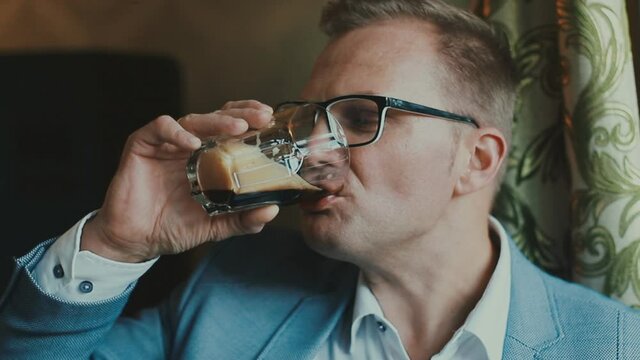 A young guy in a suit is funny and emotionally drinking a carbonated drink from a glass and licks his lips deliciously. Businessman fooling around on camera