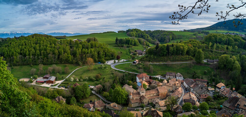 Panorama d'un village Suisse au pied du Jura avec les Alpes en arrière-plan.