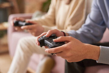 Close-up of people sitting on sofa with joysticks and playing video game in team