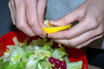 Healthy salad of leaves in a plate close-up. The girl squeezes lemon juice into a salad. The concept of diet and proper nutrition.