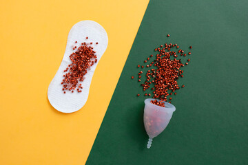 Menstrual cup full of red glitter and sanitary pad on geometric multi colored background