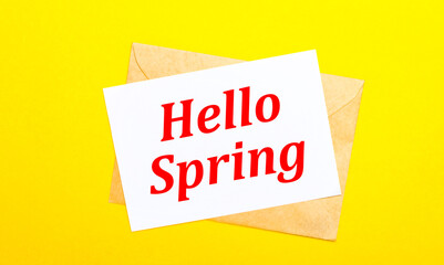 On a yellow background, an envelope and a card with the text HELLO SPRING. View from above