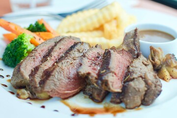 A medium-cooked steak in a white plate with fries and vegetables.