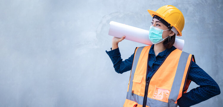 A young Asian engineer holds a white board sign for writing messages or announcements against a backdrop of concrete wall at the job site. Leader concept