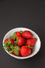 fresh large garden strawberries lie in a white bowl on a dark background