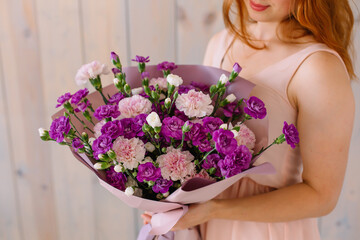 Bouquet of Violet-pink carnations and Shabo carnations in female hands on a wooden background Woman in a pink festive dress