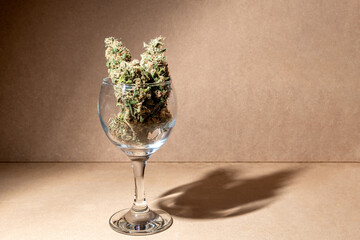 Details of medical marihuana buds ready for consumption inside a crystal glass. Selective focus on brown background.