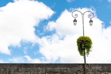 Very striking lantern with two arches, has placed some colorful flowers. It is on the right side of the image. Blue sky background with clouds.