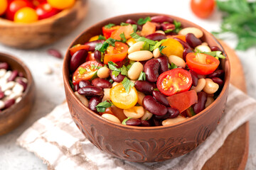 Salad of white and red beans, tomatoes and herbs in a ceramic bowl close-up. Tasty vegan food