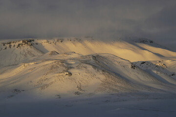 snowy mountain range lighted by sun on a cloudy day in the icelandic highlands