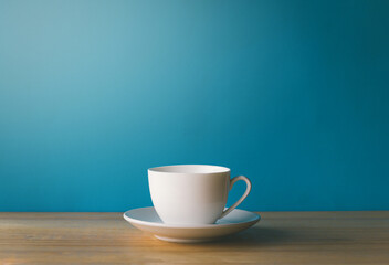 White coffee cup on wooden desk with blue background