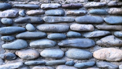 stone masonry made of round river cobblestones bonded with concrete mortar as an element of external decorative design in the style of a village or country, textured backdrop made of natural component