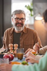 Mature bearded man sitting at dining table during lunch with his family