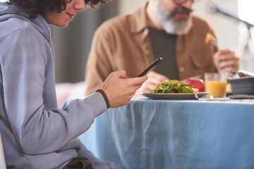 Close-up of boy sitting at dining table and using mobile phone during dinner