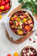 Salad of white and red beans, tomatoes and herbs in a ceramic bowl on a gray concrete table. Tasty vegan food