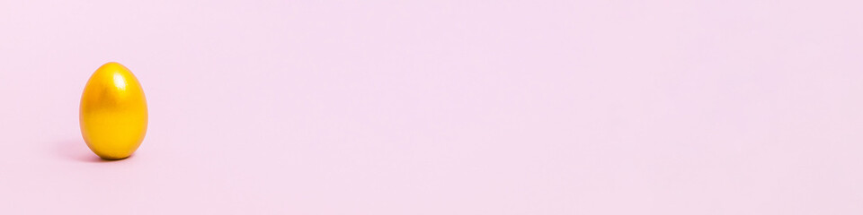 Easter egg decorated with gold paint on a pink background. Concept for Easter, spring. Selective focus. Copy space. Banner.