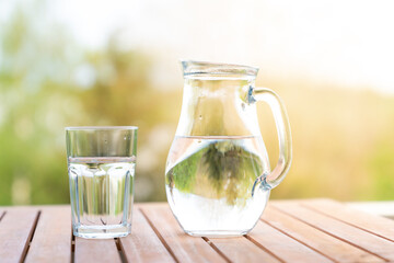 jug with water and a glass on a wooden table on the nature in the garden