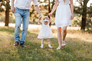 View on toddler. mother, father hold hands daughter enjoy nature and walk in the summer park. Young family spending time together on vacation, outdoors. Mother's, father's, baby's day