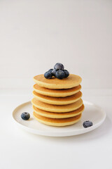 Freshly cooked soft delicious gluten free pancakes stacked on white plate, served with fresh bilberries, close up. Space for text. Healthy sweet food.