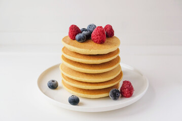 Freshly cooked soft delicious gluten free pancakes stacked on white plate, served with fresh berries, close up. Space for text. Healthy sweet food.