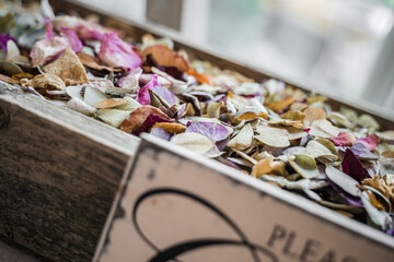 Naklejka na ściany i meble Close up of wooden rustic shabby chic box filled with confetti made of natural flower petals all different vibrant colours with sign in front asking wedding guests to take some