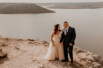 loving couple wedding newlyweds in white dress and suit walk in summer on mountain above river