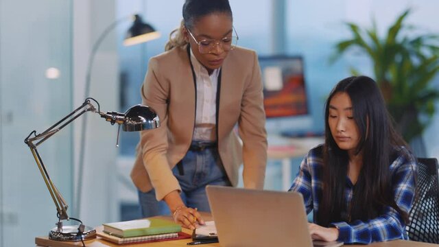 Afro-american female boss communicating with assian pretty creative manager girl checking computer project coworking in the office.