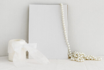 A blank white greeting card, a sprig of eucalyptus and a pearl necklace on a white background. Romantic background for the invitation.