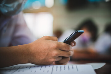 Uniform students are test exam and study online by using smartphone and wearing protective facemask in classroom