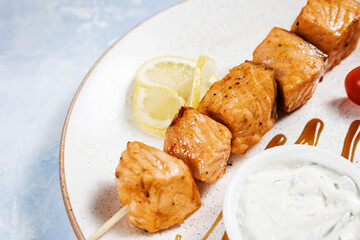 fish kebab with lemon and sauce on a white plate on a blue background