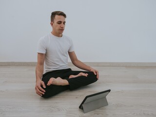 Young man doing Yoga at home with a digital tablet