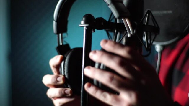 Close-up hands of unrecognizable singer taking off headphones of rack for microphone at music record studio. Closeup view of artist taking on headphones and starting to record a song in sound studio.